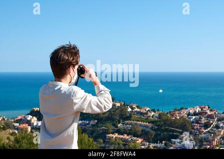 Back view of a young male wearing a facemask using binoculars looking at the sea Stock Photo
