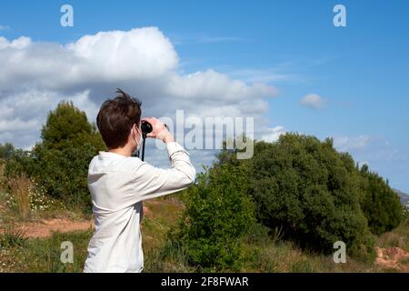 Side view of a young male using binoculars against the cloudy blue sky in a park Stock Photo