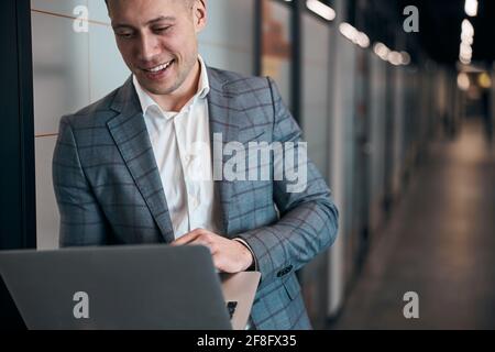 Joyful young man using laptop in office corridor Stock Photo