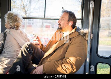 Man in public transport sitting with smartphone listening to the music Stock Photo