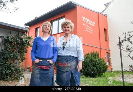 Berlin, Germany. 13th Apr, 2021. Bookbinder Julia Flögel (l) and assortment bookbinder Frauke Grenz stand in front of their paper workshop Friedrichshagen in Aßmannstraße 58. Here they repair a wide variety of damage to books, letters, documents, cards, travel cases, boxes as well as pictures. They also produce books as one-offs or in smaller editions and offer numerous courses. The shop is located in an old print shop with old drawers full of metal type, as well as machines for embossing, cutting and binding. Credit: Jens Kalaene/dpa-Zentralbild/ZB/dpa/Alamy Live News Stock Photo