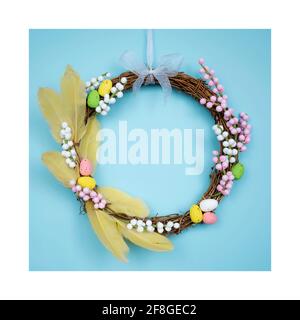 Easter wreath with yellow feathers, white and pink twigs and painted eggs on a light blue background Stock Photo