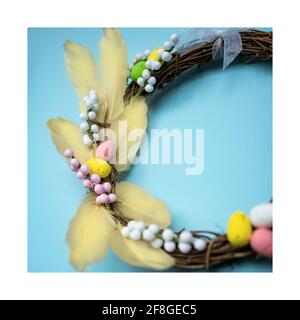 Easter wreath with yellow feathers, white and pink twigs and painted eggs on a light blue background Stock Photo
