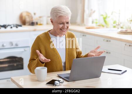 Cheerful senior woman having online class, talking to teacher Stock Photo