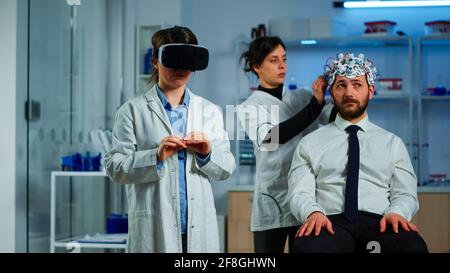 Advanced neurological scientist using medical inovation in lab wearing virtual reality glasses, gesticulating. Team of researchers working with equipment device, future, medicine, healthcare, vision, simulator Stock Photo