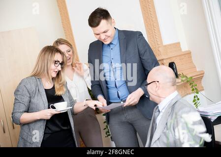 Business people are using gadgets, drinking coffee, talking and smiling while working in modern office Stock Photo