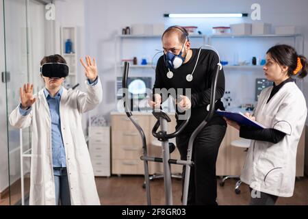 Team of scientist using virtual reality technology, in sports lab science. Professional young athlete sports endurance, cross training test with mask exercise. Stock Photo