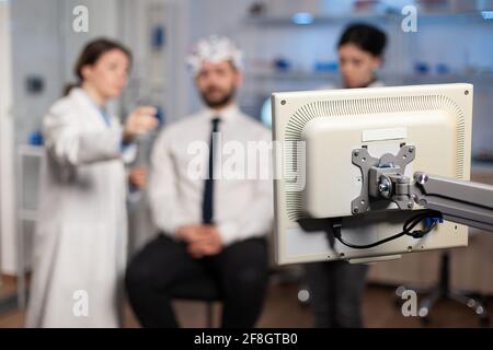 Scientist in brain study discussing with patient attached wot electrod sensors, nervous system evolution. Medical team in clinic using scanner, tomography. Stock Photo