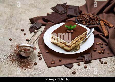 Portion of Traditional Italian Tiramisu dessert and coffee beans on grey concrete background Stock Photo