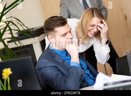 We already have great results! Young beautiful woman pointing at laptop with smile and discussing something with her coworker while standing at office Stock Photo