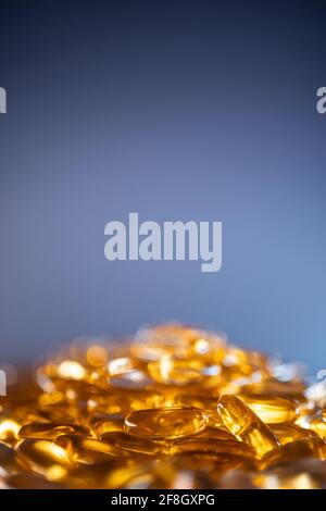 handful of golden fish oil capsules omega 3 vitamins on blue background Stock Photo