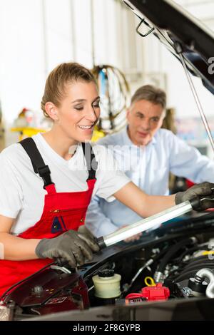 Mature man - client - and young female car mechanic looking under auto hood Stock Photo