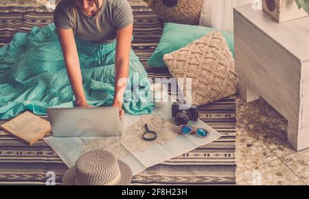 Caucasian woman planning vacation travel with laptop and map guide at home, female people plan next holidays vacation while relaxing on the floor - pr Stock Photo