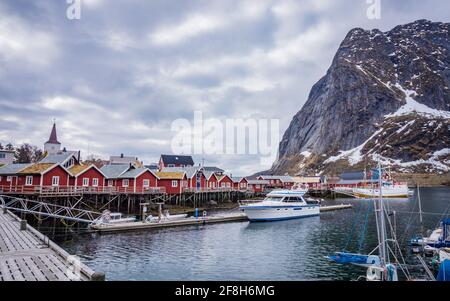 Typical red houses of Reine Fishing Village, Lofoten Islands, Norway. No people. Harbor with boats and mountain in snow. Stock Photo