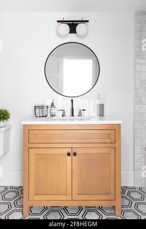 A beautiful bathroom with a wood vanity, custom tile shower and floor, and a sliding glass door with black hardware. Stock Photo