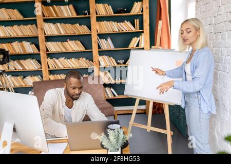 Stylish male and female colleagues working together on project, using laptop, searching ideas for startup. Multiracial business partners developing Stock Photo
