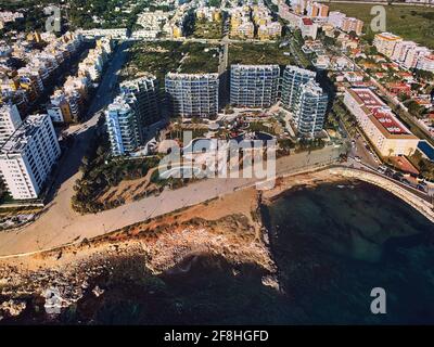Drone point of view Punta Prima seaside with rocky coastline and modern residential buildings complex at sunny summer day.  Travel and tourism of Spai Stock Photo
