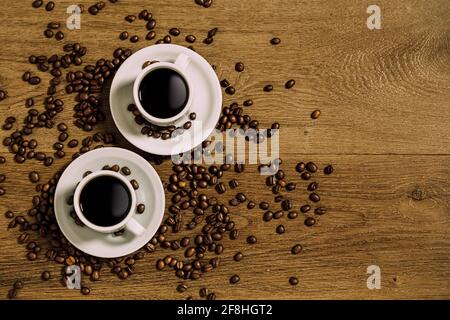 Top view of two white coffee cup over a wooden table with scattered coffee beans. Stock Photo