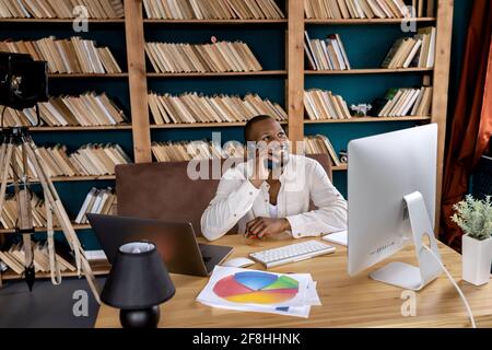 Happy male freelancer sitting at the desk in home office, having a phone conversation with colleague, smiling. Stylish african american businessman Stock Photo
