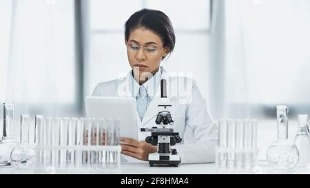 african american scientist in glasses using digital tablet near microscope in lab Stock Photo