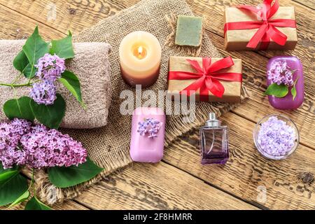 Terry towel, soap and sea salt for bathroom procedures, a burning candle, gift boxes, a bottle of perfume and lilac flowers on sackcloth and old woode Stock Photo