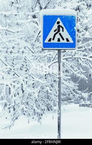 Pedestrian crossing sign in wintertime with trees covered with snow after snowfall on the background. Stock Photo