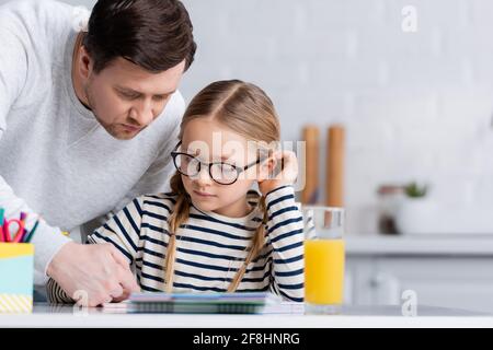 father helping daughter doing homework in kitchen, blurred foreground Stock Photo