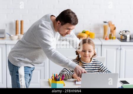 man pointing at laptop near daughter during online lesson at home Stock Photo