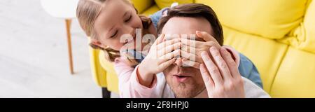 happy child covering eyes of surprised father while having fun at home, banner Stock Photo