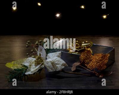 A silver-colored package with a golden rosette is given as a gift with decorations and fairy lights in the background Stock Photo