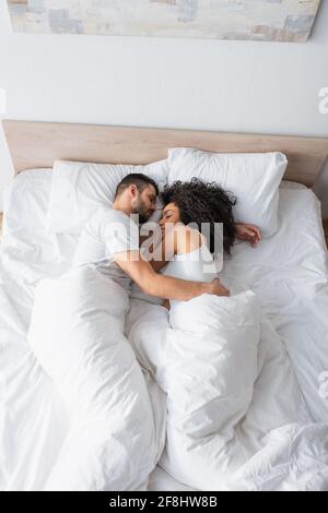 top view of interracial couple hugging and sleeping in bed Stock Photo
