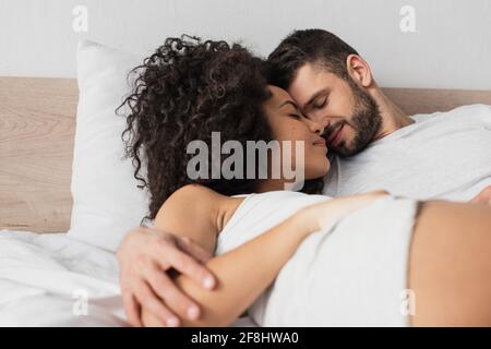 cheerful interracial man and woman hugging while lying in bed Stock Photo