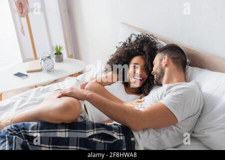 cheerful interracial couple smiling and lying on bed