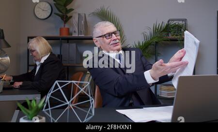 Elderly man feels lucky and glad to achieve goal while reading documents, financial papers in office Stock Photo