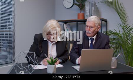 Elderly man boss with woman colleague working in office, developing new project on laptop, team work Stock Photo