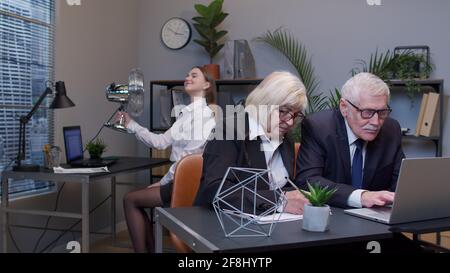 Elderly man boss with woman colleague working in office, developing new project on laptop, team work Stock Photo