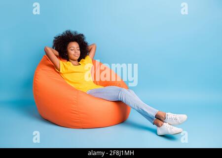 Full size photo of dark skin little brown haired girl sit sleep bean bag isolated on blue color background Stock Photo