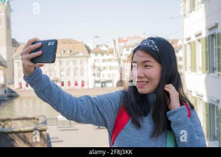 Asian woman backpacker touring in Europe - young happy and pretty Chinese girl with student backpack taking selfie with mobile phone during holidays i Stock Photo