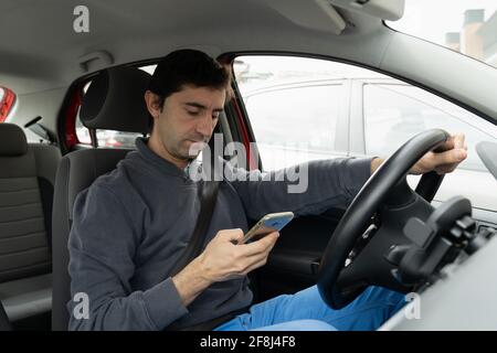 Young man driving car looking at cellphone on hand. Driver reckless behavior concept Stock Photo