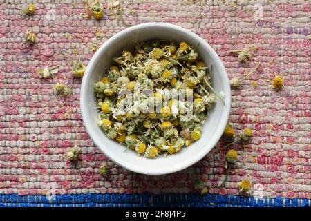 Dry chamomile flowers in a bowl on woven cotton rustic pink fabric, from above overhead top view, flat lay, closeup, naturopathy, homeopathy and natur Stock Photo
