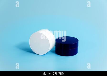 Two closed plastic cream jars on light blue background. Blank white and blue cosmetic containers. Day and night facial care concept Stock Photo