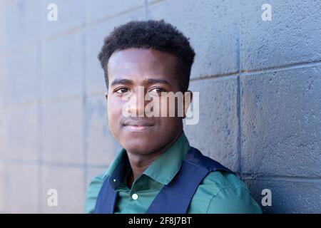 A handsome young black man leans against a gray concrete block wall Stock Photo