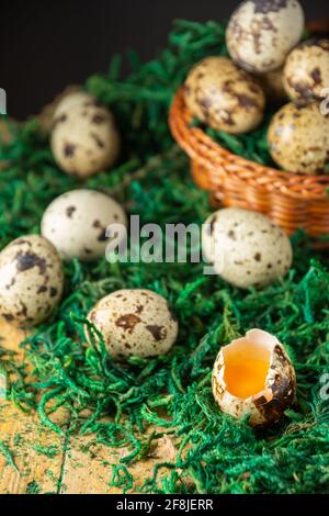 Top view of basket with quail eggs on green grass and rustic wooden table, selective focus, black background, vertical Stock Photo