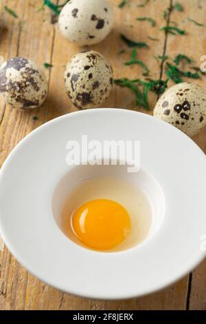 Aerial view of quail egg yolk in white plate on wooden table with more eggs, selective focus, vertical Stock Photo