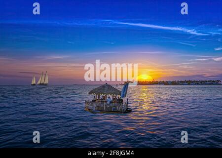 A floating tiki bar drifts along the water at sunset in Key West, Florida. Stock Photo