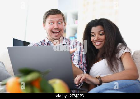 Young man and woman are sitting in front of laptop screen and smiling Stock Photo