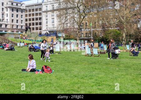 People relax in deck chairs, sunbathe and enjoy picnics in Green Park, London, England, UK Stock Photo