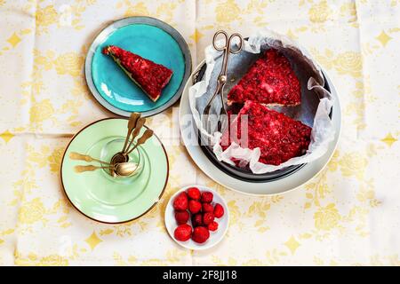 Overhead view on table with plate and cake form with red fruit cakes, empty dirty plate with spoons, strawberries on small plate. Stock Photo