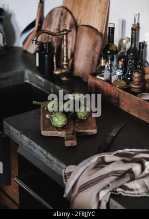 Fresh green baby artichokes on wooden cutting board in the kitchen Stock Photo