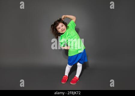 Photo of little boy girl child soccer player in sports uniform. Shows workout on a gray background in the studio. Sport concept for kids Stock Photo